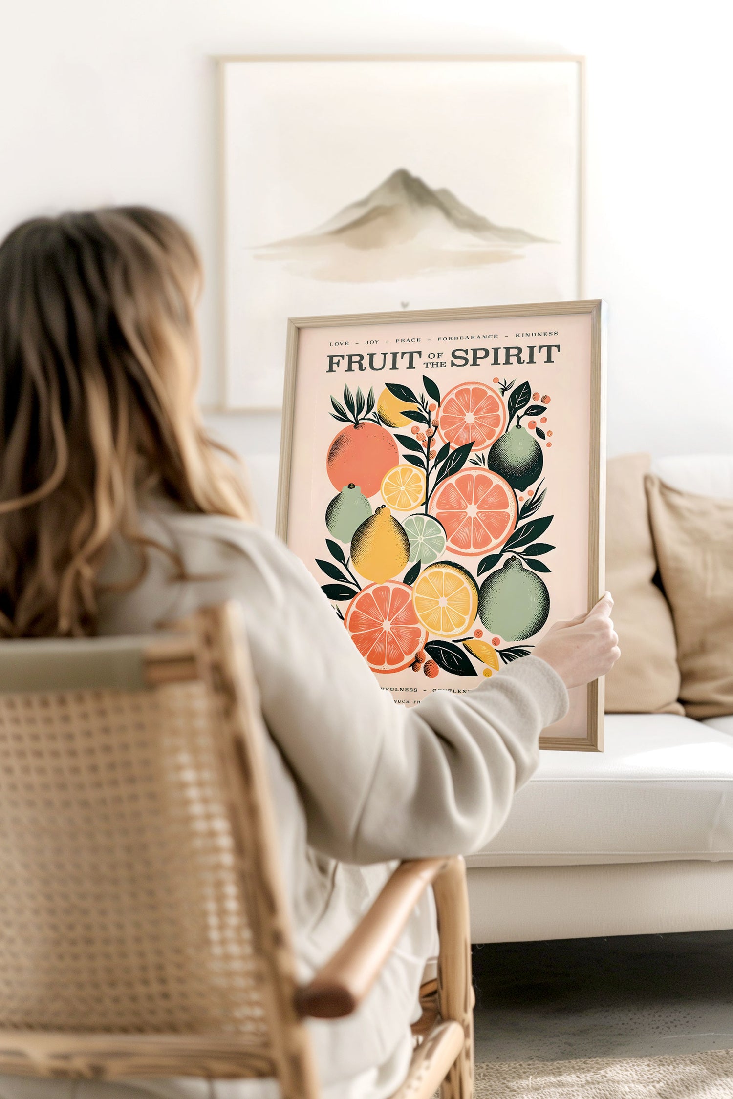 Woman holding a framed Fruit of the Spirit wall art print featuring vibrant citrus fruits and biblical virtues like love joy and peace in a cozy minimalist living room setting adding a pop of color and Christian inspiration to the decor